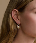 Close-up of a person wearing a pearl earring with a neutral background