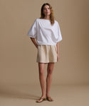 Woman wearing a white blouse and beige shorts against a beige background.