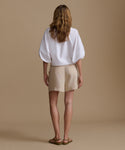 Woman wearing a white blouse and beige shorts against a beige background.