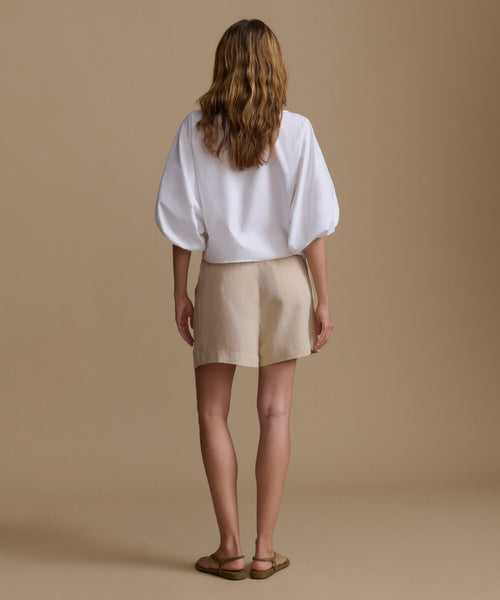 Woman wearing a white blouse and beige shorts against a beige background.