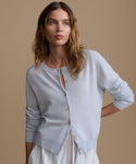 Woman wearing a light blue cardigan with blue and white stripe shorts against a beige wall.