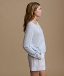 Woman wearing a light blue cardigan with blue and white stripe shorts against a beige wall.