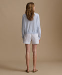 Woman wearing a light blue cardigan with blue and white stripe shorts against a beige wall.