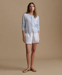 Woman wearing a light blue cardigan with blue and white stripe shorts against a beige wall.