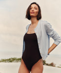 Woman wearing a light blue cardigan with a black bathing suit at the beach.