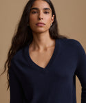 A woman wearing a navy blue V-neck knit sweater, photographed against a solid warm beige studio background.