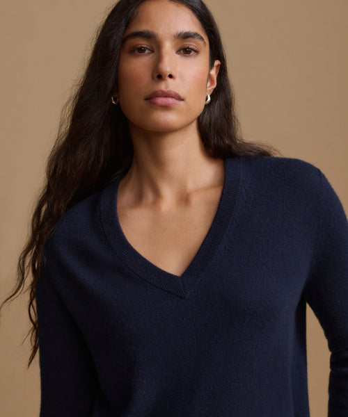 A woman wearing a navy blue V-neck knit sweater, photographed against a solid warm beige studio background.