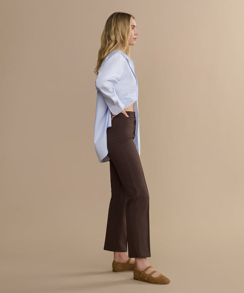 Woman wearing a light blue shirt and brown pants against a beige background