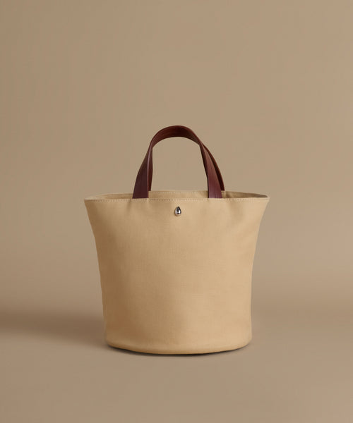 Beige tote bag with brown handles on a beige background