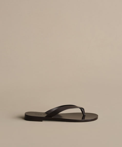 A single Gia Sandal in black with a simple strap design is shown on a plain beige background—ideal for effortless summer style.