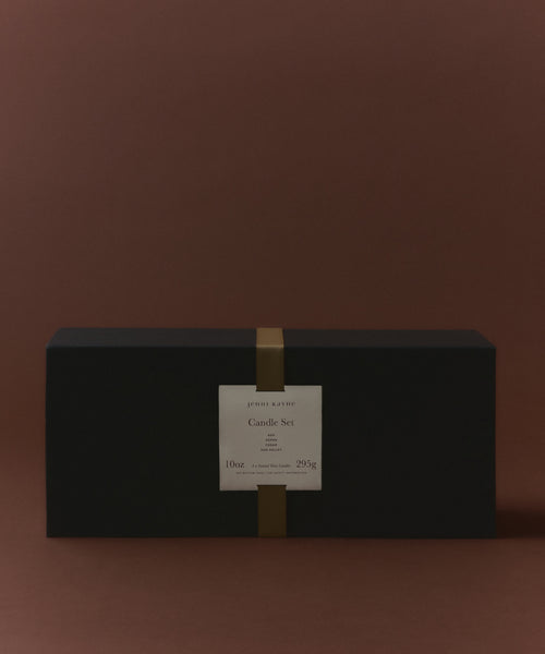 A rectangular black box with a gold vertical band and a white label reading Glass Candle Gift Set sits against a plain brown background, presenting an elegant candle gift set perfect for fans of scented candles.