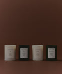 The Glass Candle Gift Set displays four minimalist candles (two white, two black) in a row on a brown background, each labeled with a unique scent: Ash, Aspen, Cedar, and Sun Valley.