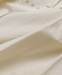 A close-up of light beige Italian cotton poplin on the Harper Dress shows buttons and small embroidered eyelets near the top—an elegant detail.