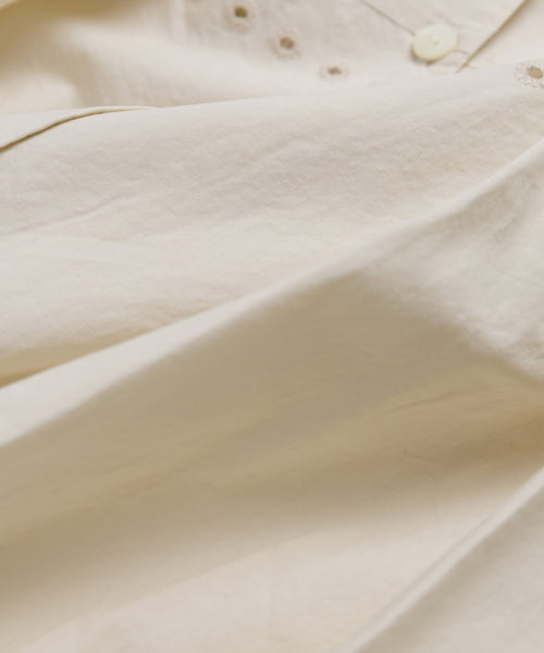 A close-up of light beige Italian cotton poplin on the Harper Dress shows buttons and small embroidered eyelets near the top—an elegant detail.