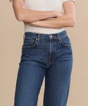 A person in a white short-sleeve shirt and Harper Jean—a relaxed mid-rise, wide-leg style—stands with arms crossed against a plain beige background.