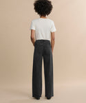 A person with curly hair faces away, wearing a white short-sleeve t-shirt and the Harper Jean—relaxed mid-rise, wide-leg jeans—against a plain beige background.
