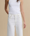 A person wearing a white sleeveless top and high-waisted Harper Jean stands against a beige background, with one hand behind their back and the other relaxed by their side.