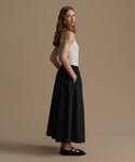Woman wearing a white top and black skirt against a beige background