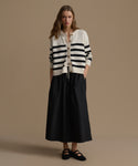 Woman wearing a striped cardigan and black skirt on a beige background