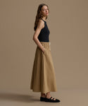 Woman wearing a black top and beige pants against a brown background