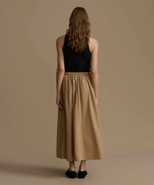 Woman wearing a black top and beige skirt against a brown background