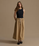 Woman wearing a black top and beige skirt against a brown background