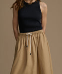 Woman wearing a black sleeveless top and tan drawstring skirt on a brown background