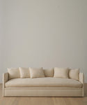 The Dume Sofa in beige hemp, with five matching cushions, stands against a light wall on a pale wooden floor, featuring eco-friendly, sustainable hemp upholstery for a minimalist touch.