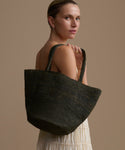 Woman holding an olive woven bag against a beige background
