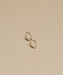 The Iris Diamond Hoops are small 14k gold earrings with subtle embedded stones, elegantly displayed on a smooth beige surface.