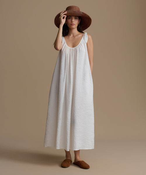 Woman wearing a white dress and brown hat against a beige background