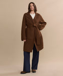 A person stands against a plain beige background, wearing the Jessica Sweater Coat over a white top and navy wide-leg pants.