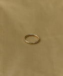 The June Baguette Band from Jenni Kayne Jewelry, a simple diamond yellow gold ring, is centered on a plain beige fabric background.