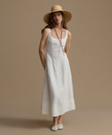 Woman wearing a white dress and beige hat against a brown background