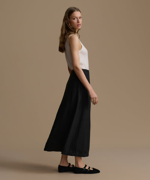 Woman wearing a white top and black pants against a beige background