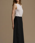 Woman wearing a white sleeveless top and black pants on a beige background