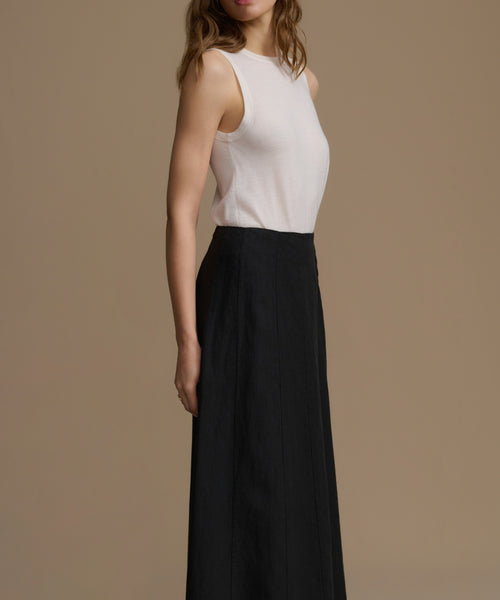 Woman wearing a white sleeveless top and black pants on a beige background