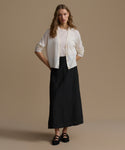 Woman wearing a white blouse and black skirt against a beige background