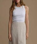 Woman wearing a white tank top and beige skirt against a brown background