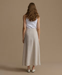 Woman wearing a white top and beige skirt against a brown background