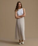Woman wearing a sleeveless white top and beige skirt against a brown background