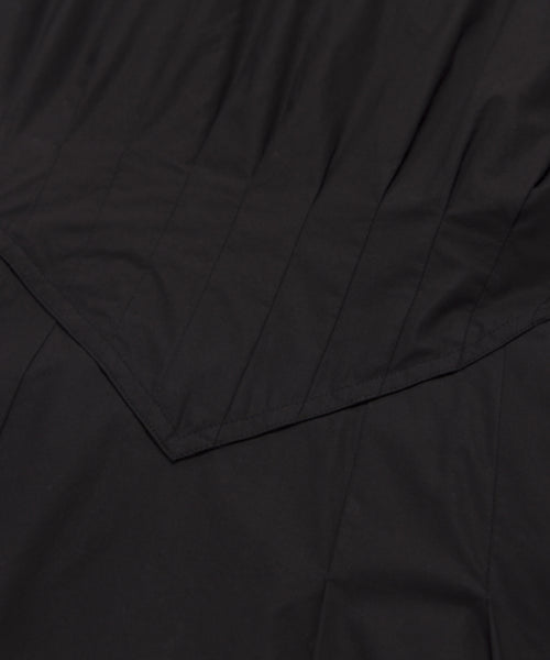 Close-up of black fabric with visible stitching and pointed, layered seam detail. The smooth, slightly shiny material hints at a refined summer staple—perfect for the Kit Dress.