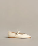 The Lana Flat is a cream-colored Mary Jane shoe with a tapered toe and thin strap featuring a silver buckle, displayed against a plain light beige background.