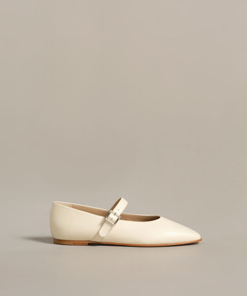 The Lana Flat is a cream-colored Mary Jane shoe with a tapered toe and thin strap featuring a silver buckle, displayed against a plain light beige background.
