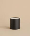 The Large Aspen Glass Candle features two wicks and white wax in a matte black holder. Hand-poured in Los Angeles, it sits on a neutral beige surface with a matching background.