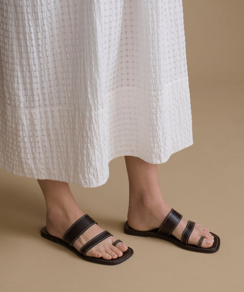 Person wearing black sandals and a white textured skirt on a beige background