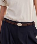 A person styles a white t-shirt with high-waisted navy blue pants and the Leather Audrey Belt—a brown calf leather belt with an oval silver buckle.
