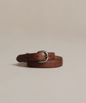 The Classic Belt, expertly crafted in Italy from nappa leather and featuring a silver buckle, is coiled and displayed on a plain light beige background, adding timeless elegance to any wardrobe.