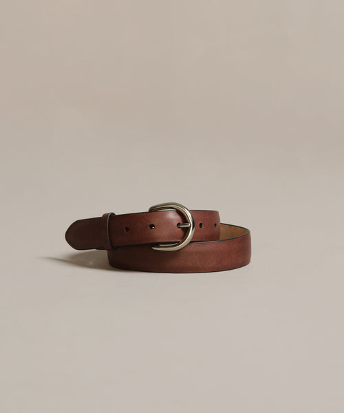 The Classic Belt, expertly crafted in Italy from nappa leather and featuring a silver buckle, is coiled and displayed on a plain light beige background, adding timeless elegance to any wardrobe.