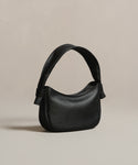 The Loren Shoulder Bag is crafted from soft pebbled leather with a curved top, wide strap, and subtle textured finish, shown against a neutral beige background.